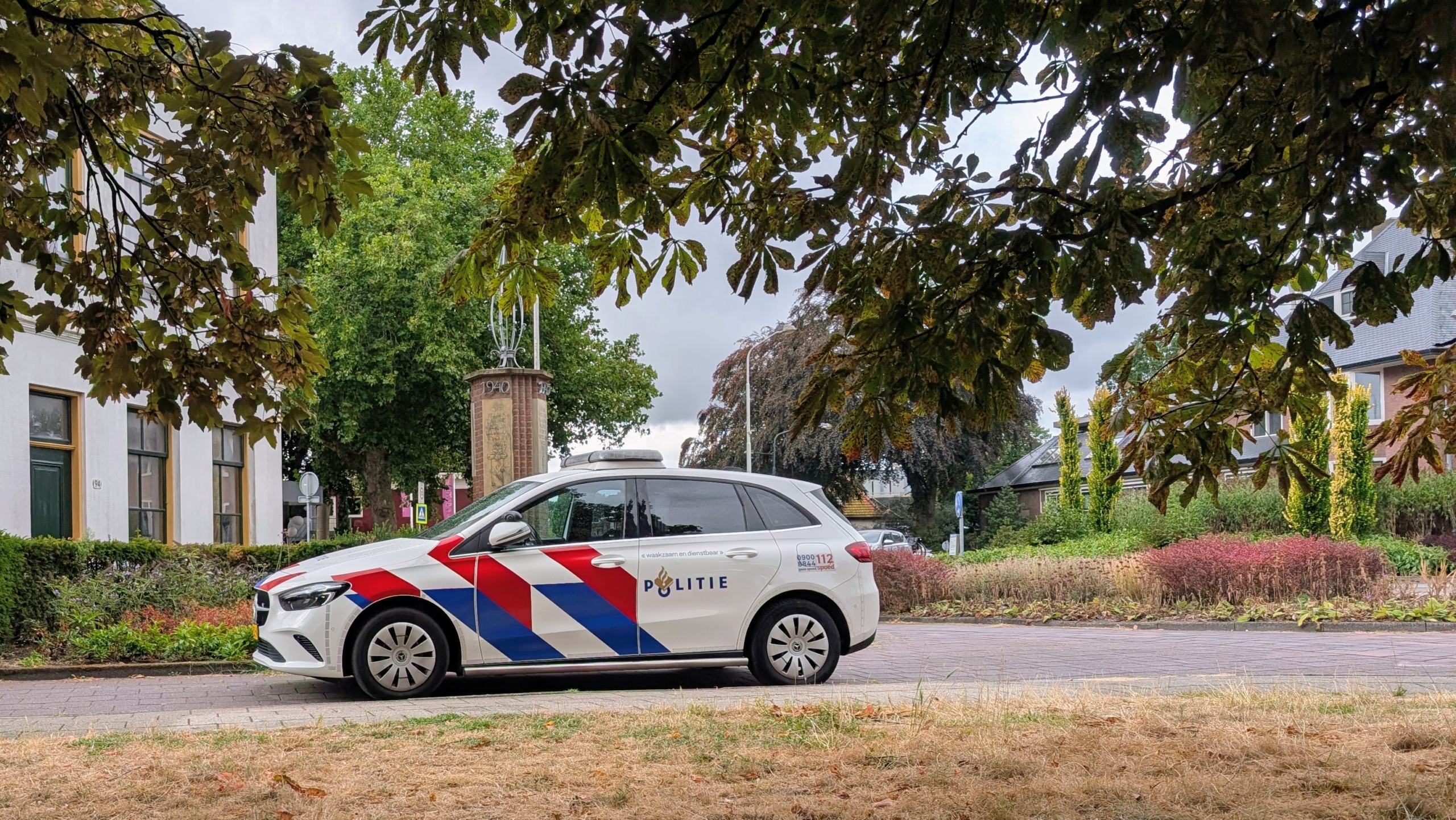 Politieagenten bij een donkergrijze politiebus voor een gebouw, met afzetlint op de voorgrond
