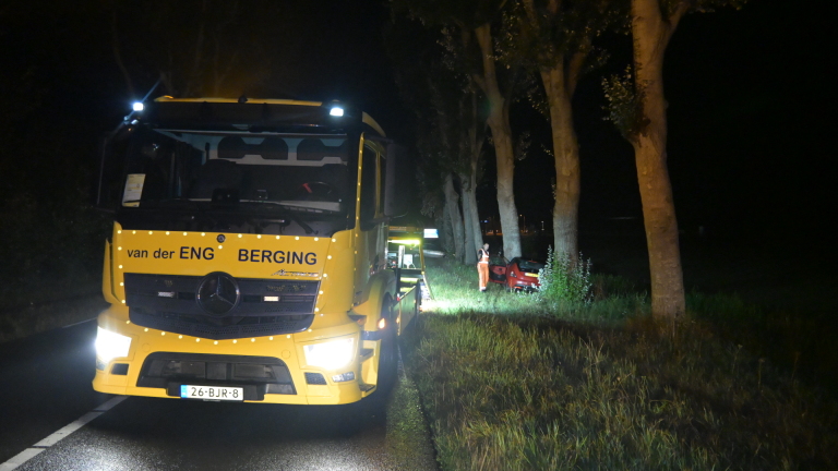 Ambulance en politievoertuigen met zwaailichten op een donkere weg, hulpverleners bij een auto in de berm