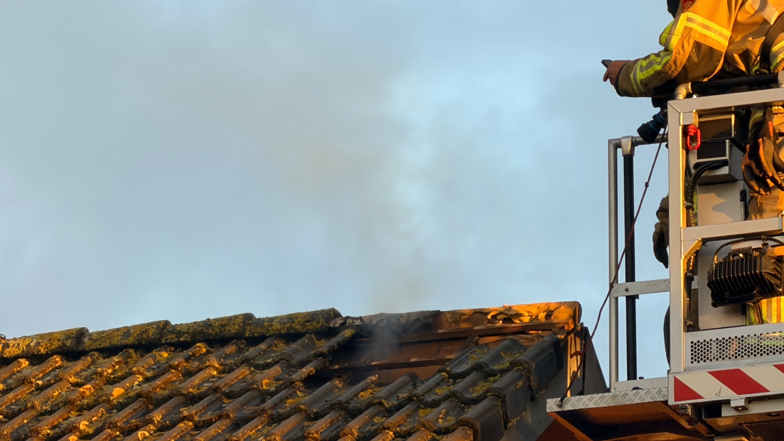 Politie en omwonenden kijken toe terwijl brandweer met hoogwerker een dak van een woonhuis inspecteert