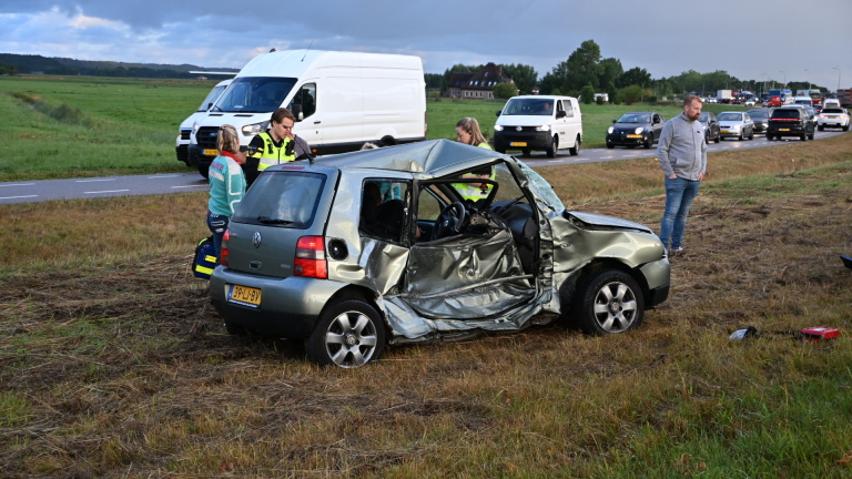 Politieauto met zwaailicht blokkeert rijstrook met pionnen; gele hulpdienstauto en vrachtwagens staan stil in file