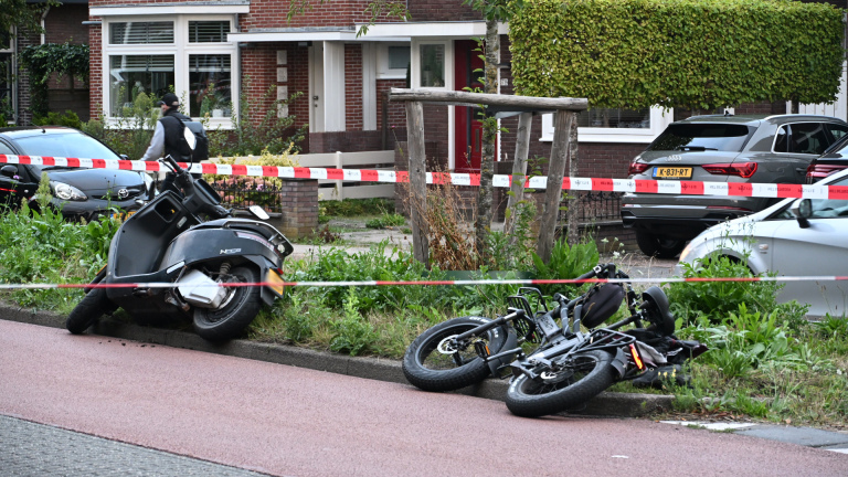 Politieagent bij afgezet ongeval op woonstraat, met omgevallen motor op de weg en politielint ertussen