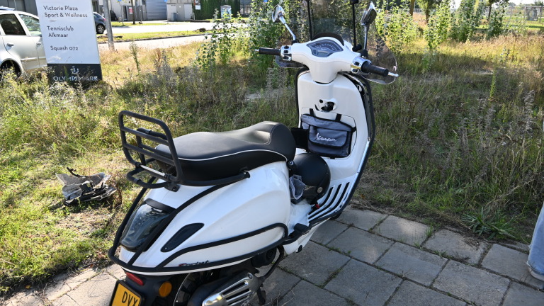 Gele ambulance en politieauto geparkeerd langs een fietspad; fietsers passeren op een zonnige dag