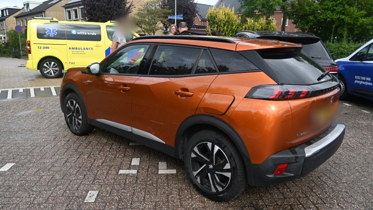 Oranje SUV geparkeerd op nat wegdek met op de achtergrond een gele Witte Kruis-ambulance en omstanders