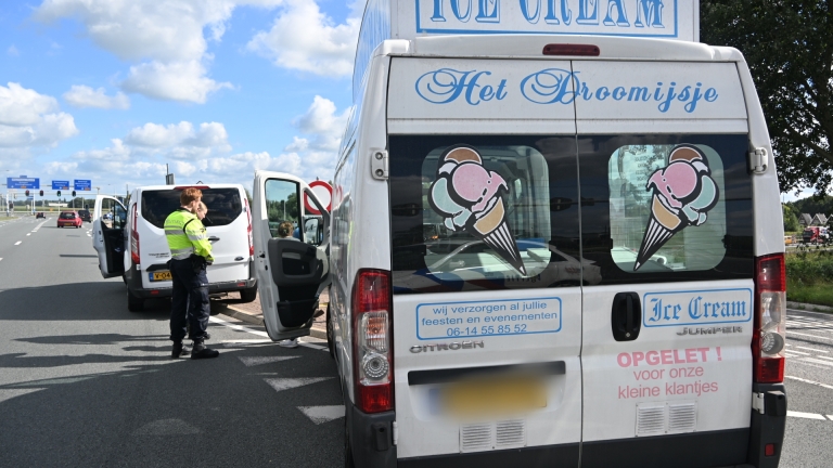 IJswagen met bord Ice Cream Car staat stil bij kruispunt, naast een witte bestelbus en politie op de weg