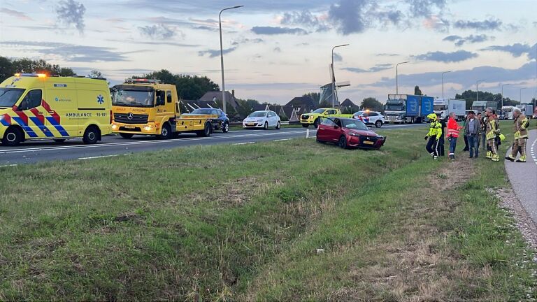 Twee beschadigde auto’s in de berm na aanrijding langs de snelweg, met hulpdiensten en verkeer op de achtergrond