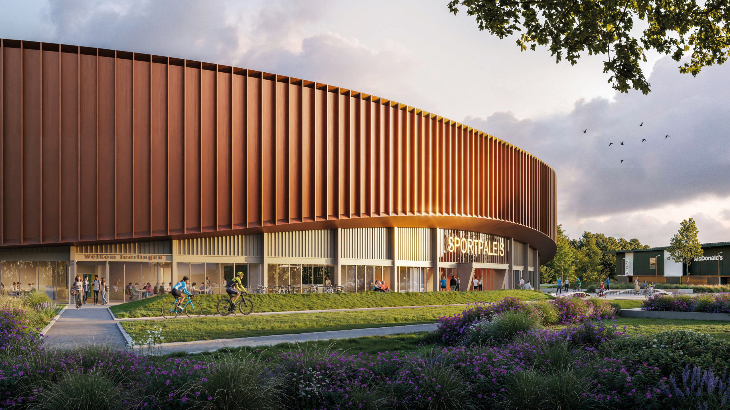 Modern rond sportpaleis met roodbruine gevel, mensen en fietsers bij de entree, omringd door groen en bloemen