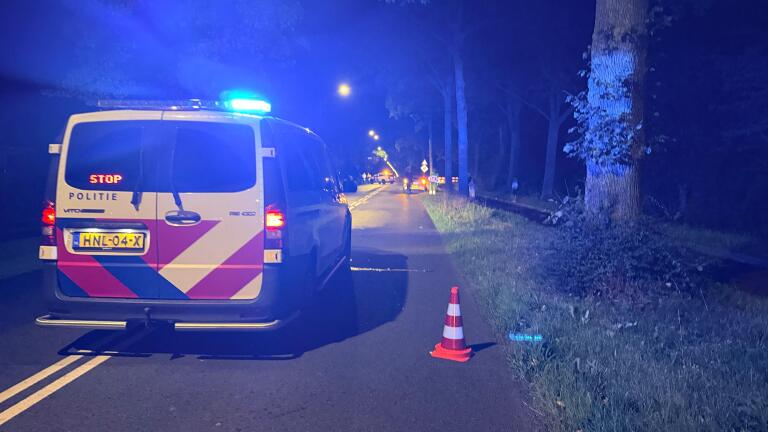 Politiebus met blauwe zwaailichten en STOP-display blokkeert ’s nachts een weg met verkeerskegels