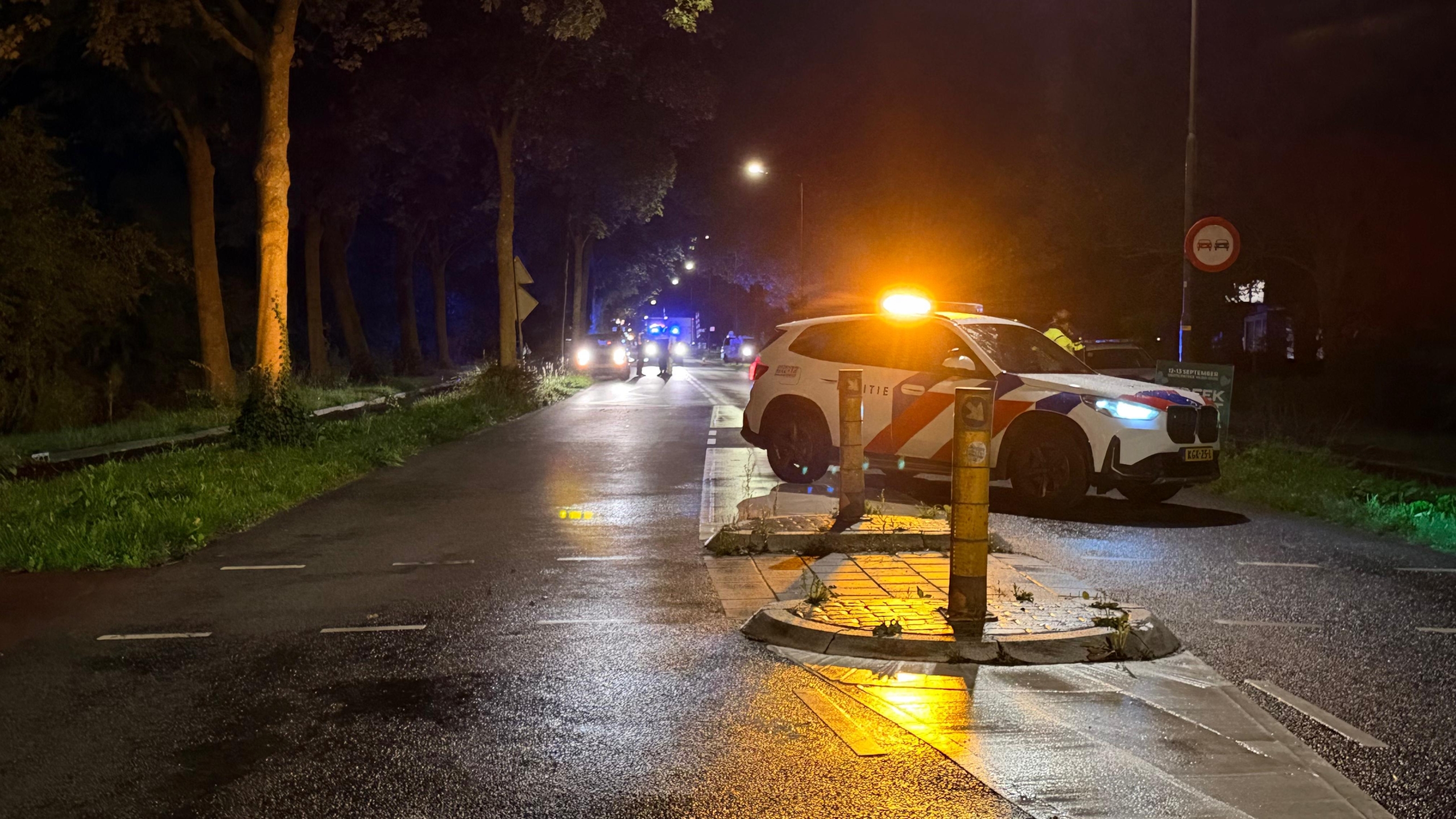 Politiebus met blauwe zwaailichten en STOP-display blokkeert ’s nachts een weg met verkeerskegels