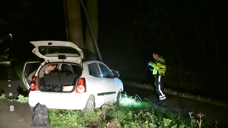 Politieagent met zaklamp bij witte auto met open achterklep, stilstaand langs een donkere weg