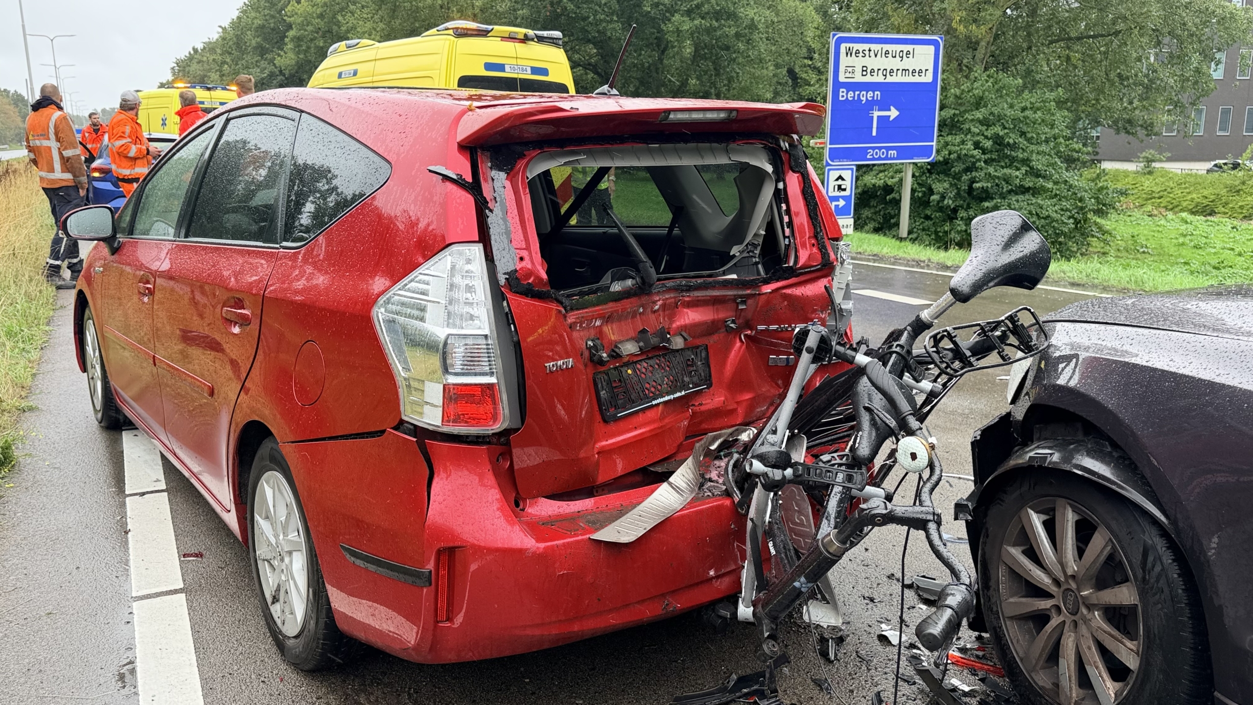 Botsing op natte weg tussen zwarte bestelbus en Audi, met zichtbare schade en hulpdiensten op de achtergrond
