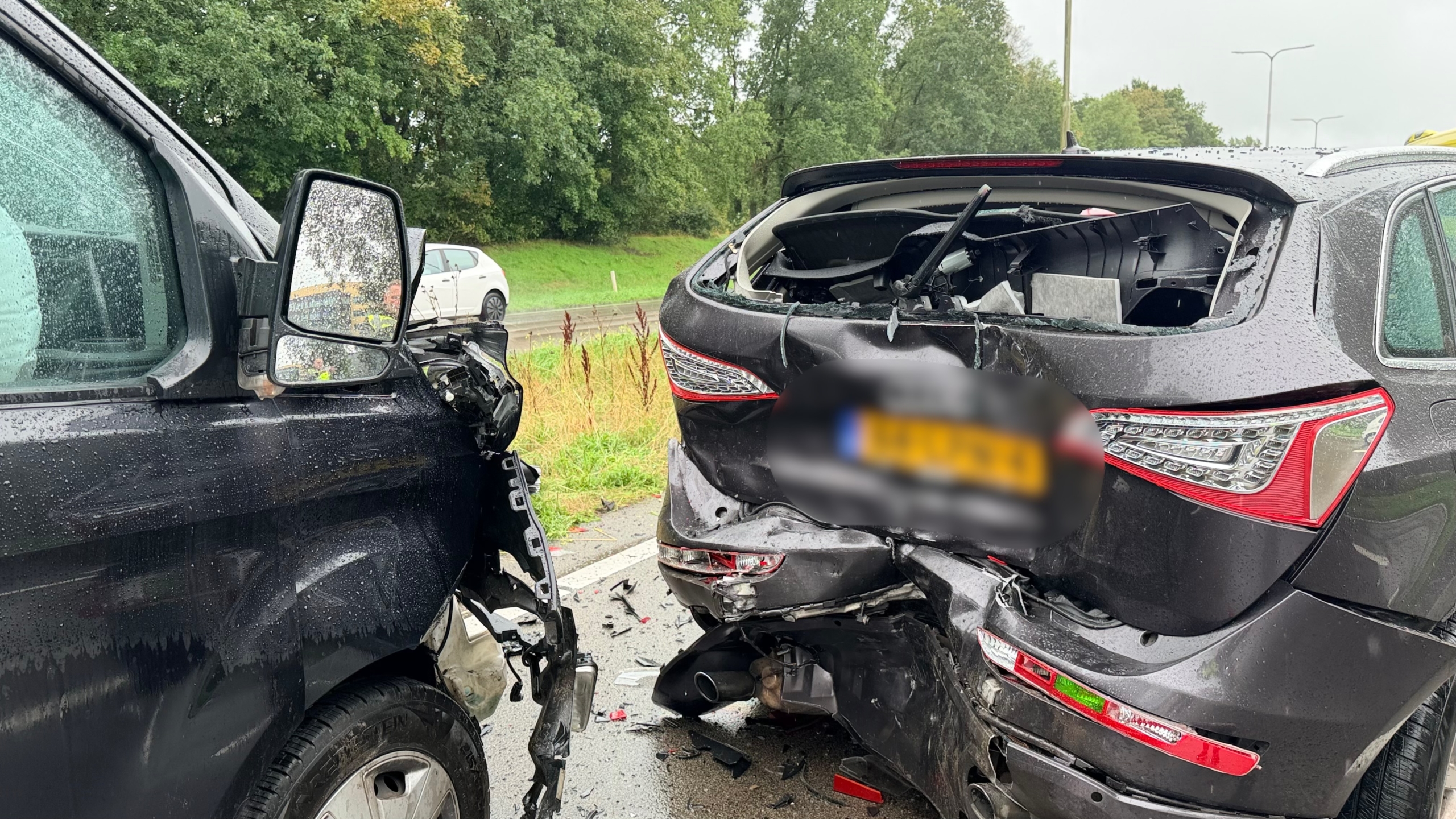 Botsing op natte weg tussen zwarte bestelbus en Audi, met zichtbare schade en hulpdiensten op de achtergrond
