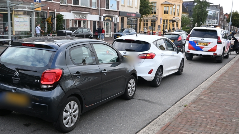Politieauto en ambulance staan op straat naast een witte bestelbus, met een agent ertussen bij een gebouw