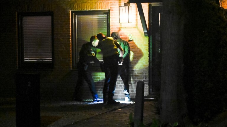 Twee agenten staan ’s nachts op straat tussen politievoertuigen met zwaailichten