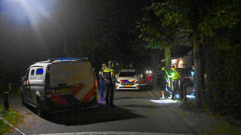 Twee agenten staan ’s nachts op straat tussen politievoertuigen met zwaailichten
