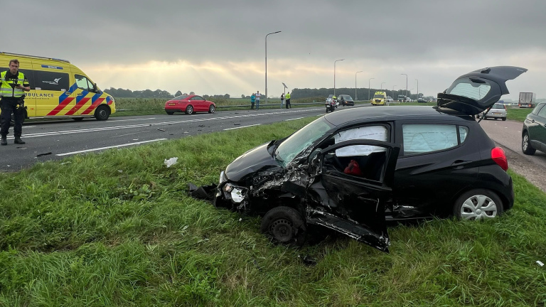 Beschadigde witte bestelbus in de berm naast de snelweg, met hulpdiensten en andere auto’s verderop