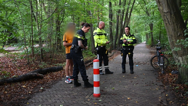 Drie politieagenten spreken met een man op een bospad; een fiets staat tegen een boom