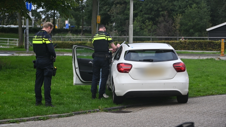 Ambulance en twee agenten bij witte auto die deels op het gras staat in een woonwijk