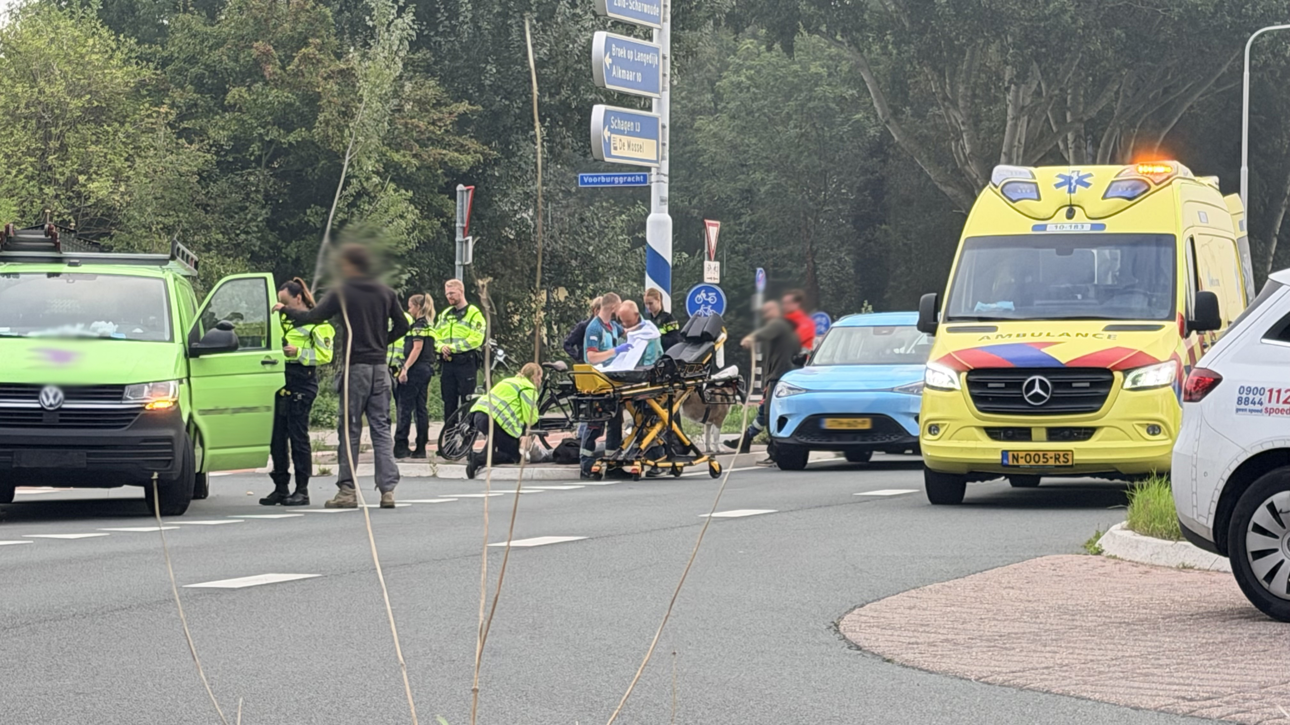 Hulpdiensten bij verkeersincident: politie, ambulance en brancard met afscherming naast een fiets op kruispunt