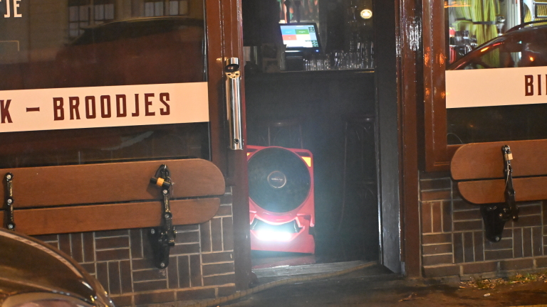 Brandweerlieden en politie op straat bij een hoekpand in de nacht, met brandweerwagen, slangen en fietsen op de voorgrond