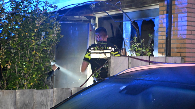 Brandweer en ambulance met zwaailichten bij een woongebouw ’s nachts, met brandweerlieden op straat