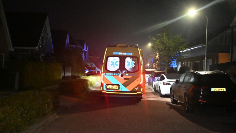 Brandweer en ambulance met zwaailichten bij een woongebouw ’s nachts, met brandweerlieden op straat