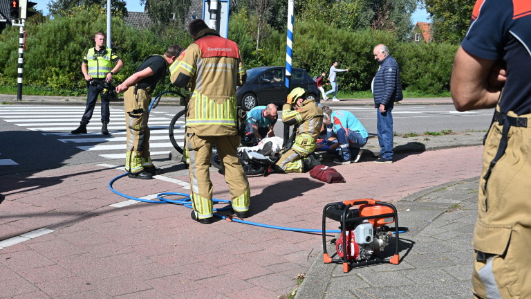 Brandweerwagen, politieauto en ambulance staan bij een kruispunt terwijl hulpverleners iemand op straat verzorgen
