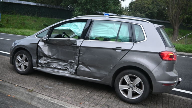 Beschadigde lichtblauwe auto wordt weggesleept na ongeval, met Nederlandse politieauto’s en agenten op kruispunt