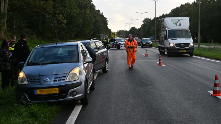 Politieagent en wegwerker regelen verkeer bij een stilstaande auto langs de weg, met pionnen en pechhulpwagen