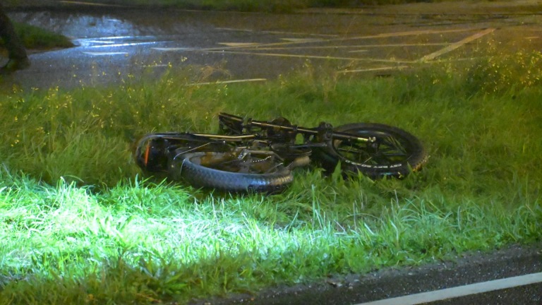 Politie en hulpverleners onderzoeken ’s nachts een ongevalslocatie langs de weg, met een omgevallen fiets in het gras