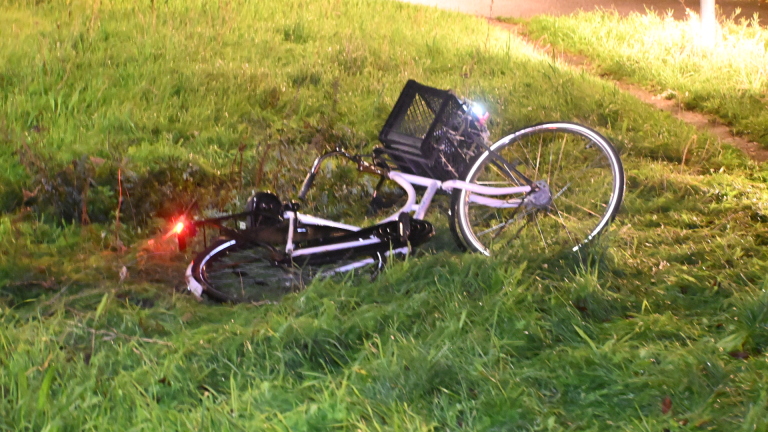 Afgezette ongevalslocatie met beschadigde auto en omgevallen fiets in het gras, met hulpverleners in de achtergrond