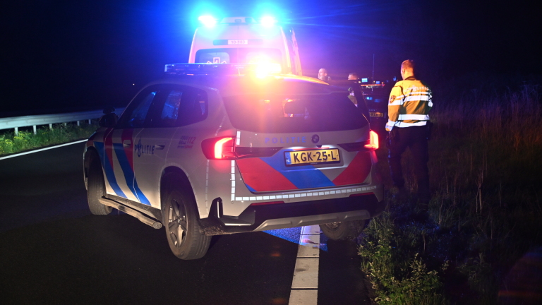 Zwarte auto na aanrijding langs de weg, met uitgeklapte airbag en schade aan de linker voorkant, in blauw zwaailicht