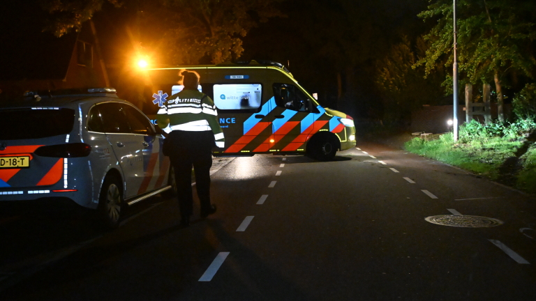 Donkere auto in de berm bij struiken, met op de achtergrond een witte caravan bij een huis in het donker