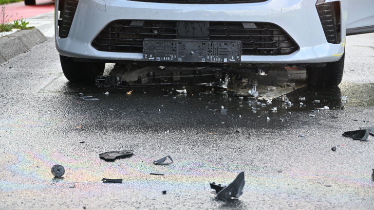 Politieagent praat met bestuurder naast grijze auto met open portier bij kruispunt met rood licht en brokstukken op weg