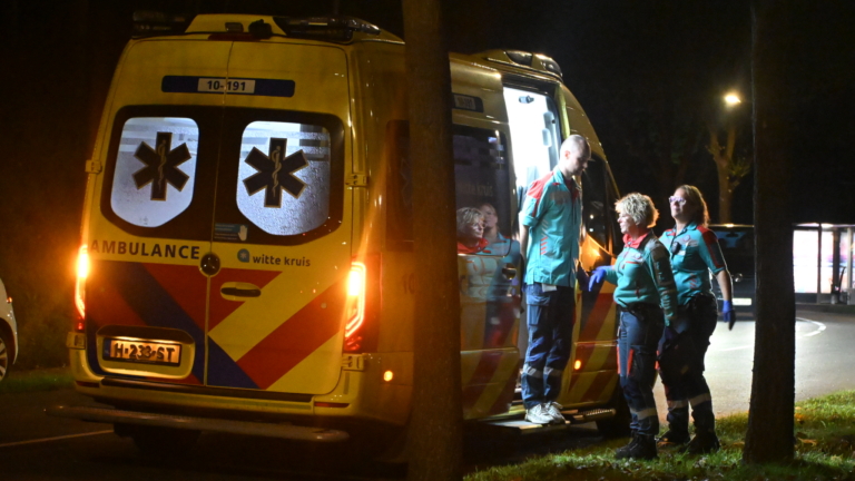 Ambulance in de nacht met geopende deur; drie hulpverleners staan bij het voertuig langs de weg