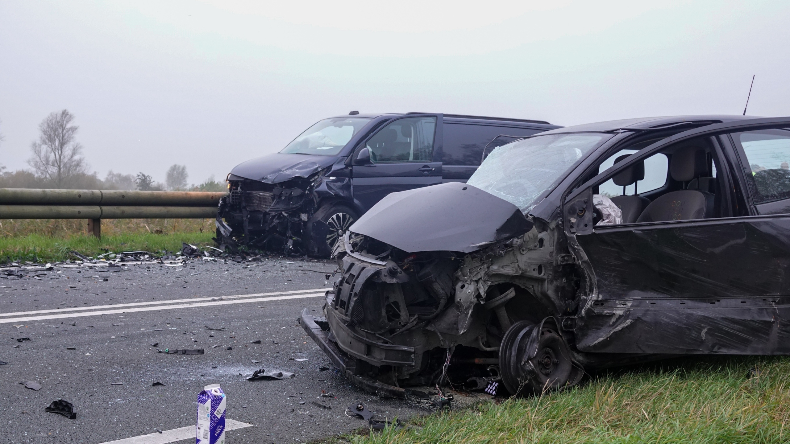 Twee politieauto’s en een ambulance met zwaailichten op een landelijke weg, met molens op de achtergrond