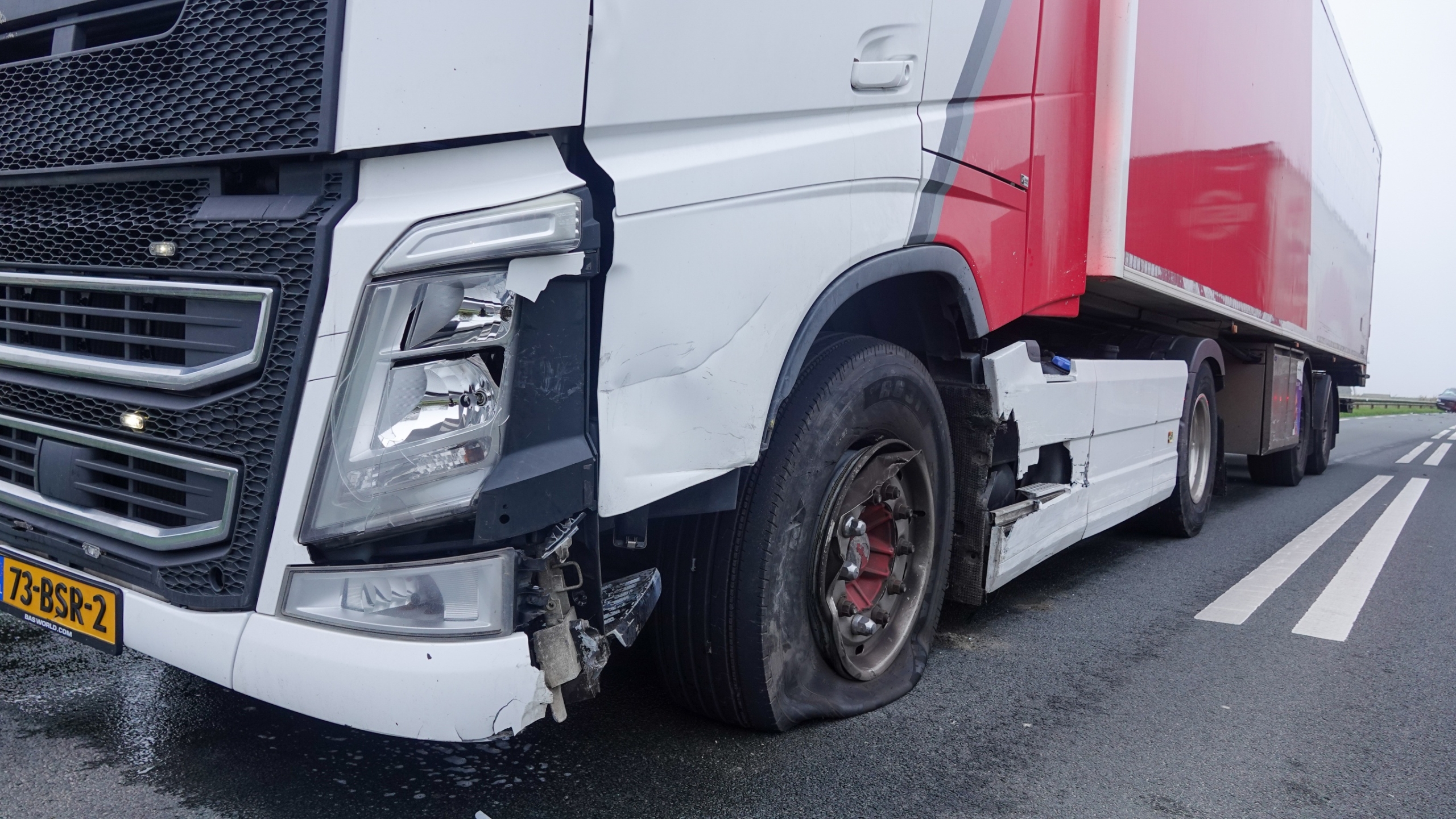 Twee politieauto’s en een ambulance met zwaailichten op een landelijke weg, met molens op de achtergrond