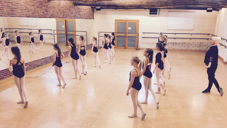 Balletles met jonge dansers in een studio met spiegels en een leraar.