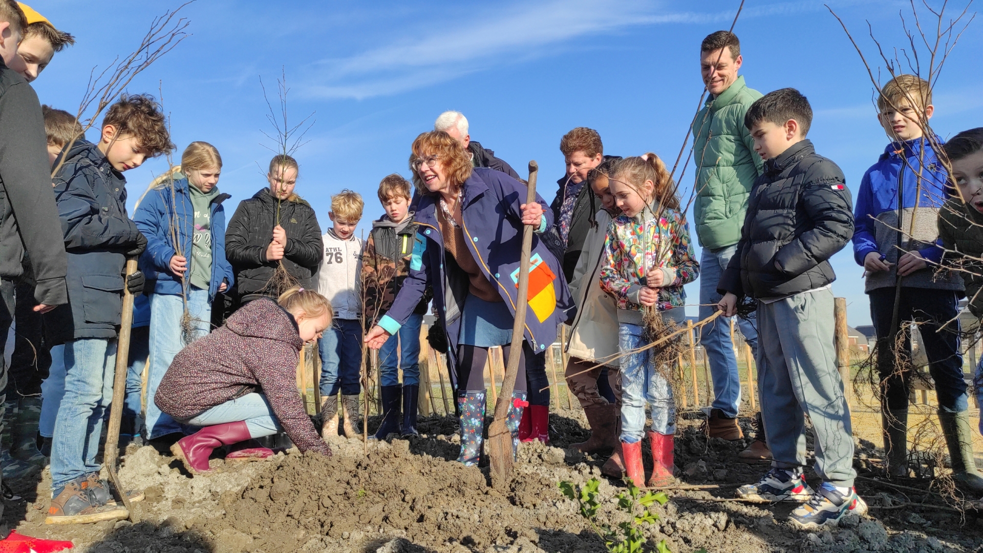 Wethouder Anjo van de Ven plant een boom met een schoolklas om haar heen.