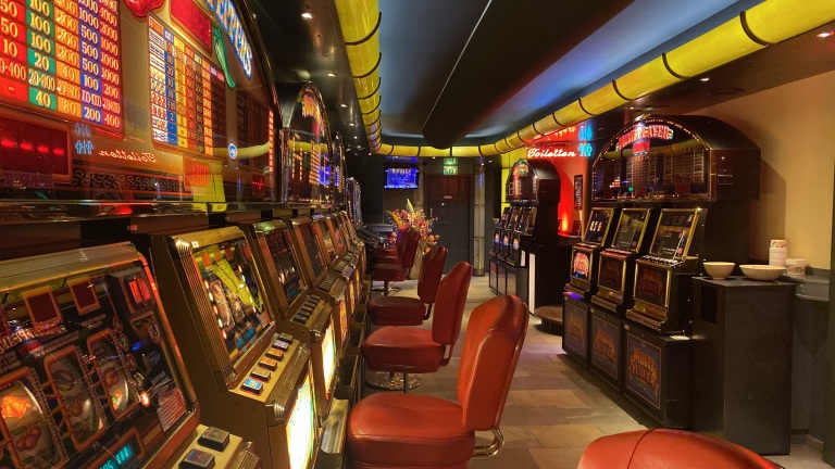 Interieur van een casino met speelautomaten en rode stoelen in een verlichte omgeving.