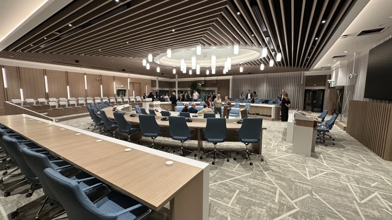 Moderne vergaderruimte met ovale tafel, blauwe stoelen en hanglampen, waar mensen bijeen zijn.