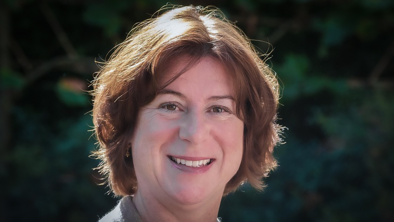 Portret van een lachende vrouw met bruin haar, gefotografeerd met een groene achtergrond.