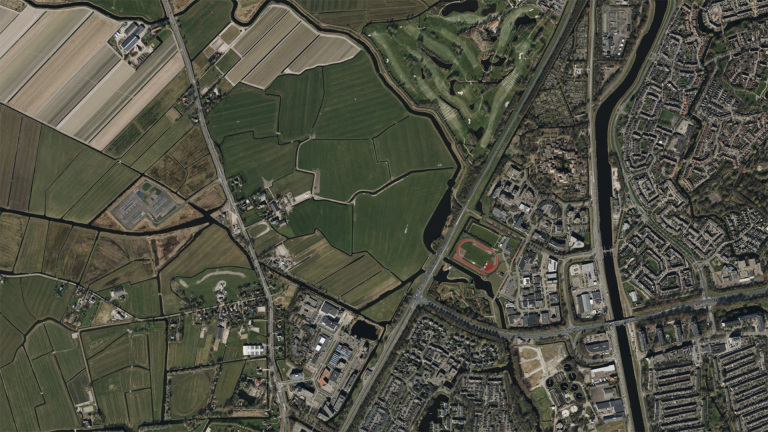 Satellietbeeld van een stedelijk gebied met woonwijken, landbouwvelden en een atletiekbaan.