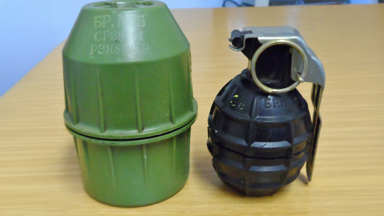 Groene plastic behuizing naast zwarte handgranaat met metalen hendel en ring op een houten tafel