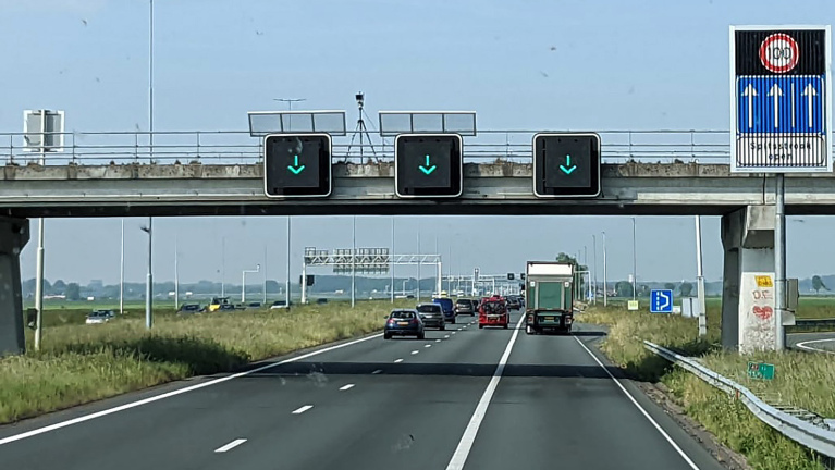 Autos rijden op een snelweg onder een viaduct met groene pijlen naar beneden op digitale borden.