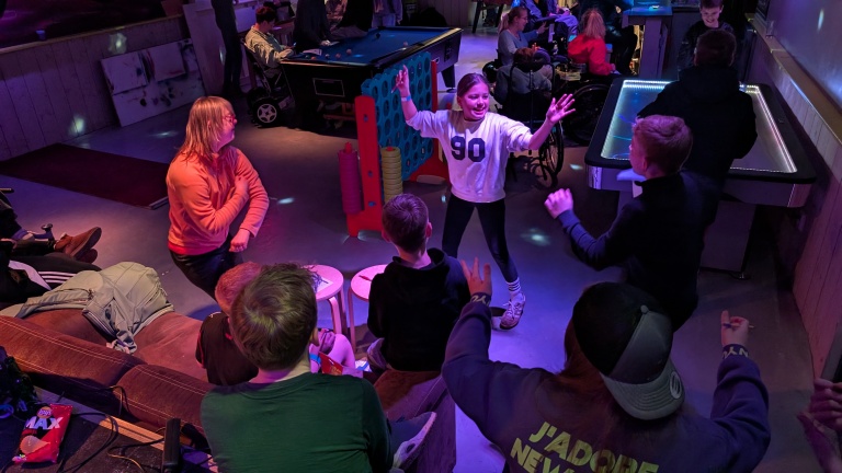 Mensen vermaken zich in een speelruimte, met een meisje dat enthousiast danst terwijl anderen toekijken.