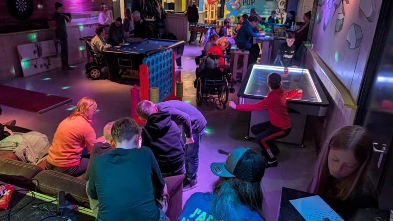 Groep mensen speelt en ontspant in een spelzaal met gezellige verlichting, met pooltafel en airhockeytafel.