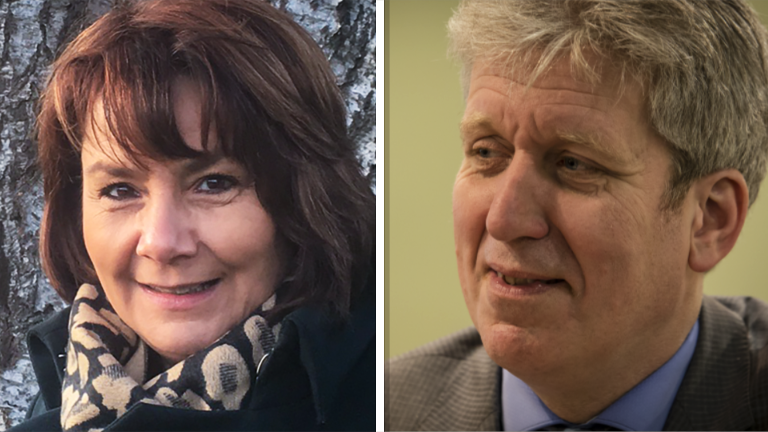 Twee personen, een vrouw in een jas met sjaal en een man in pak, beide lachen.