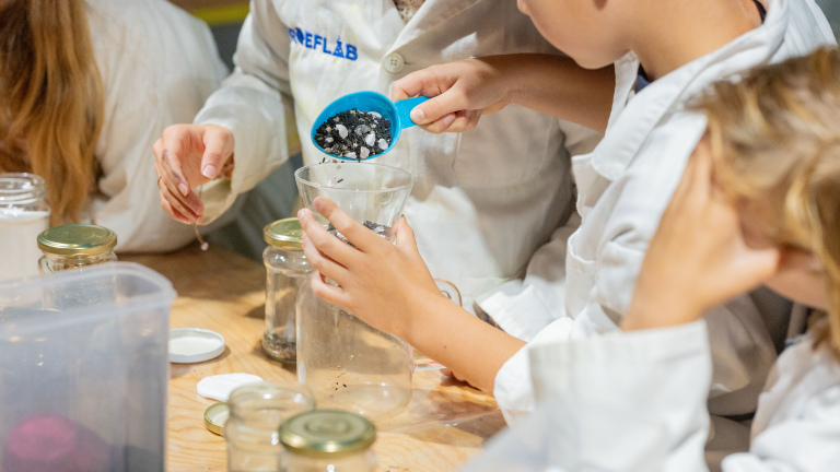 Kinderen in labjassen doen een experiment met potten en een maatbeker.