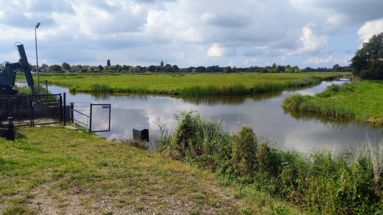 Nederlands landschap met sloten en weilanden, in de verte het dorp De Rijp
