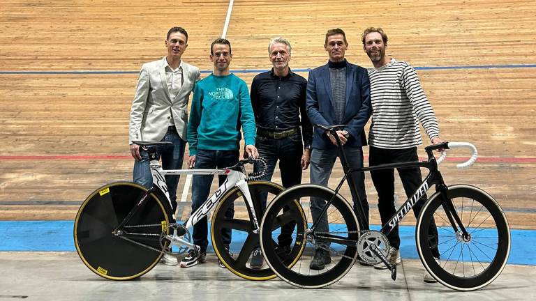 Vijf mannen poserend met racefietsen op een wielerbaan.